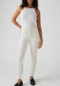 Camiseta de tirantes blanca de canalé combinada con unos jeans blancos ajustados. Los jeans presentan una textura suave y un diseño clásico de cinco bolsillos. Unos mocasines negros completan el look.