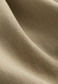Világos bézs szövet, lágy, texturált felszínnel. A szövése látható, finom szálakkal és egyenletes, sima eséssel.