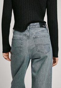 Grå denimjeans med en lös passform, med fem fickor och en svart märkeslabel på midjan. Stylad med en svart ribbad tröja.