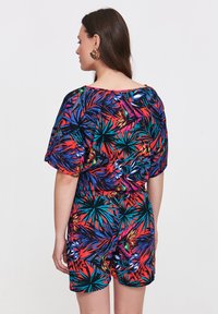 Kolorowy krótki kombinezon z krótkimi rękawami, ozdobiony żywą tropikalną grafiką w odcieniach czerwieni, niebieskiego, zielonego i czarnego, z elastycznym pasem i luźnym krojem.