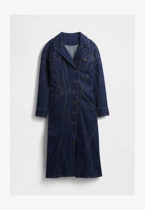 Denimkjole i mørkeblå med krave, knaplukning og to brystlommer. Har unikke syningsmønstre og lange ærmer.