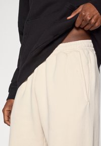 Μαύρο φούτερ με κουκούλα και τσέπη μπροστά, σε συνδυασμό με μπεζ φόρμα με κορδόνι στη μέση και πλαϊνές τσέπες. Μαλακά, υ φή υφασμάτων.