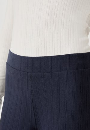 Leggings de canalé en color navy con una cinturilla ancha, confeccionados con una tela texturizada, combinados con una blusa blanca de canalé que presenta sutiles líneas verticales.