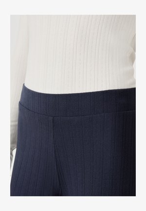 Leggings de canalé en color navy con una cinturilla ancha, confeccionados con una tela texturizada, combinados con una blusa blanca de canalé que presenta sutiles líneas verticales.