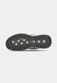 Semelle extérieure en caoutchouc noir avec motif de crampons rugueux et lugs hexagonaux surélevés ; semelle intermédiaire beige ; logo de la marque embossé au centre.