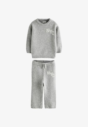 Grå stickad tröja och byxset med ribbade ärmar, med en vit "NYC"-grafik på båda delarna. Mjuk textur och avslappnad stil.