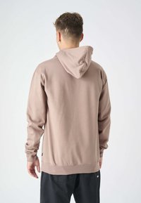Felpa con cappuccio in tessuto marrone chiaro, con maniche lunghe, vestibilità comoda e polsini a costine. Cuciture visibili all'orlo e al cappuccio.