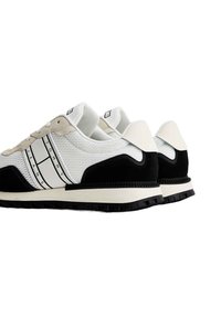 Zapatillas deportivas blancas y negras que presentan una parte superior de malla, acentos de ante, rayas características y una suela de goma texturizada.