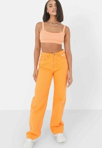 Oranje cropped tanktop en wijde oranje jeans, gemaakt van denim, met een gestructureerd ontwerp en blauwe hardwareaccenten.