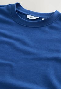 Camiseta de algodón azul marino con cuello redondo, textura suave y corte relajado. Presenta una etiqueta dentro del cuello con el nombre de la marca.