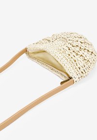 Bolso de mano tejido en tono crema con forma estructurada, correa de cuero marrón y un forro interior suave. Presenta un tejido abierto para ventilación.