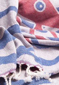 Soft woven fabric with red and blue geometric patterns and fringed edges, draped in loose folds.