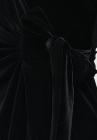 Črna žametna tkanina zbrana in zvezana v velik, mehak pentljo z gladko, puhasto teksturo in subtilnim sijajem.