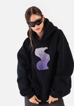Czarna bluza z kapturem z dużą, teksturowaną grafiką fal w kolorach purpurowym i białym. Posiada przednią kieszeń i przestronny, wygodny krój. Noszone modne czarne okulary przeciwsłoneczne.