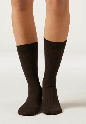 Bruna knähöga strumpor med vertikal ribbad textur och en tjock ribbad kant, tillverkade av elastiskt material för komfort.