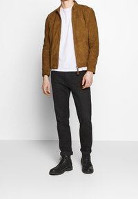 Brun mockajacka med dragkedja framtill, vit t-shirt under, svarta jeans och svarta snörkängor. Minimalistisk design, slät textur.