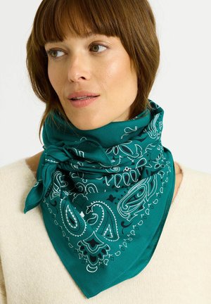 Pañuelo azul verdoso con patrones blancos de paisley y flores, hecho de tela suave, atado ordenadamente alrededor del cuello, llevado sobre un suéter claro.