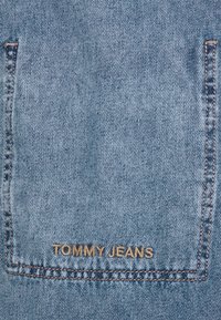 Bakfickan på ljusblå denimjeans med bruna sömmar och "TOMMY JEANS" broderat i botten av fickan.