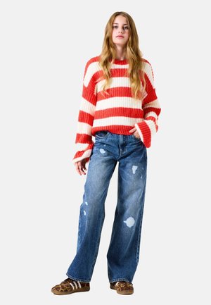 Jersey de punto de gran tamaño a rayas rojas y blancas, pantalones vaqueros anchos desgastados de color azul, y zapatos de leopardo marrón con acentos blancos.