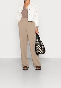 Giacca di denim bianca corta, canotta beige con pizzo marrone, pantaloni beige a gamba larga, borsa intrecciata bianca e nera, sandali piatti marroni.