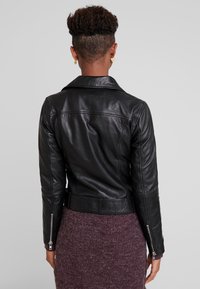 Veste de moto en cuir noir avec une coupe ajustée, col cranté et poignets zippés. Texture lisse avec une silhouette élégante.