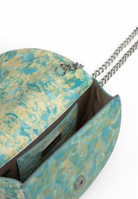 Bolso de cuero con patrón en turquesa y beige, con cadena como asa, que cuenta con un cierre magnético y un bolsillo interior. Textura suave, forma redondeada.