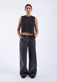 Faded black cropped denim top with raw hem, paired with loose black wide-leg jeans and a black belt featuring a square buckle.