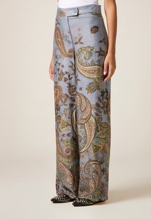 Mujer con pantalones anchos de talle alto con base azul y patrones de paisley y flores multicolor, combinados con zapatos negros puntiagudos con tachuelas.