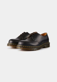 Pantofi din piele neagră cu vârful rotunjit și închidere cu șireturi. Prezintă cusături galbene pe talpa intermediară și o talpă din cauciuc durabilă cu aderență texturată.
