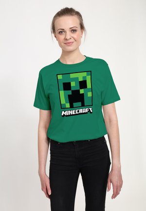 Grøn bomulds T-shirt med et firkantet Minecraft Creeper-ansigt grafisk tryk centreret på brystet, med "MINECRAFT" tekst nedenfor i hvid.