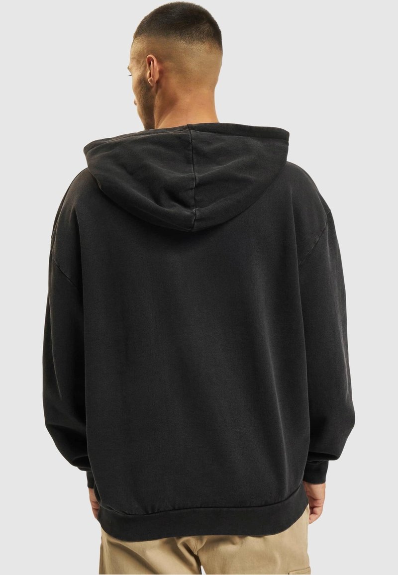 Sweat à capuche noir oversize en tissu doux avec capuche à cordon, épaules tombantes, poignets et ourlet côtelés. Design uni.