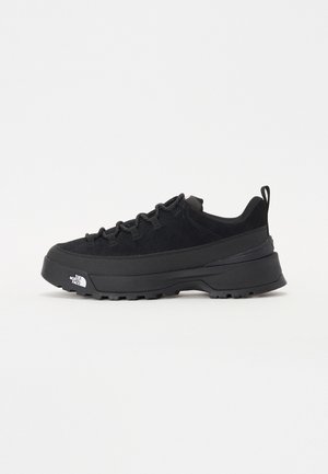 Svart utendørs sneakers med overdel i semsket skinn, teksturert gummisåle og solid snøresystem. Har forsterket hæl og merkevarelogo på siden.