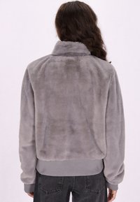 Jachetă gri din blană sintetică cu guler înalt, manșete și tiv cu nervuri. Spatele are o textură netedă, fără modele sau accente vizibile.