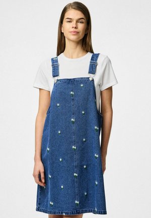 Vestido de peto de mezclilla en azul con bordado floral blanco, tirantes ajustables y corte recto, combinado con una camiseta blanca.