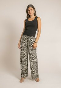 Débardeur noir à volants associé à un pantalon large à motif zèbre noir et blanc. Modèle portant des sandales métalliques à lanières.