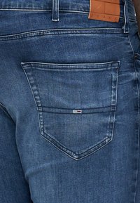 Jeans in denim blu scuro con una tasca posteriore caratterizzata da cuciture sottili e un piccolo etichetta con logo. La texture è liscia con un design a vestibilità classica.