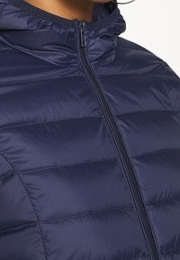 Chaqueta de plumas azul marino con cremallera frontal, cuello acanalado y textura acolchada. Material ligero con detalle de costura horizontal.