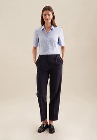 Camicia azzurro chiaro a maniche corte con bottoni abbinata a pantaloni blu navy a vita alta. Mocassini neri completano l'outfit, caratterizzati da una texture liscia.