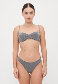 Ensemble bikini à carreaux noir et blanc comprenant un haut bandeau avec des bonnets souples et des bretelles ajustables, associé à un bas taille basse assorti.