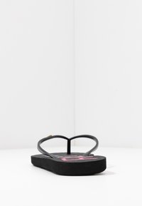 Svarte flip-flops med teksturert såle, flat fasong, smale stropper og et fargerikt grafisk design på fotsengen.