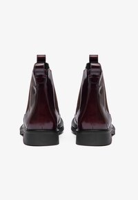 Bottines Chelsea en cuir verni bordeaux avec panneaux élastiques sur les côtés, languettes de tirage et semelles robustes en caoutchouc noir, présentant un design élégant.