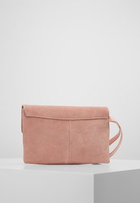 Borsa a pochette in suede rosa pallido con pattina ripiegata, design piatto, tracolla sul lato e dettaglio di cucitura visibile.