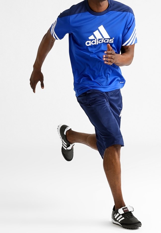 Sininen lyhythihainen urheilu paita, jossa on valkoinen Adidas-logo, yhdistettynä tummansinisiin sortseihin ja mustiin lenkkikenkiin, joissa on valkoiset raidat ja hihnakiinnitys.