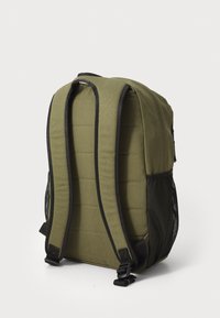 Mochila de color verde oliva con respaldo acolchado, acentos negros, correas ajustables y bolsillos laterales de malla. Tejido duradero con una forma estructurada.