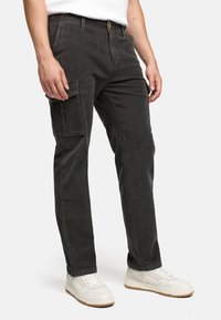 Cargo bukser i mørkegrå kordfløjl med sidelommer og lige pasform, parret med hvide sneakers. Struktureret stof med synlige ribber.