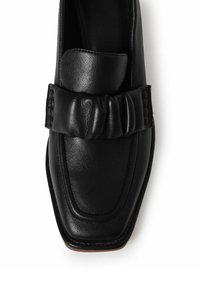 Mocasines de cuero negro con punta cuadrada, que cuentan con un detalle de correa gathered y una textura suave. La suela contrastante ofrece un acento sutil.
