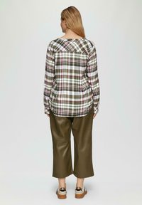 Karierter, langärmeliger Hemd in grün, weiß und pink; olivgrüne, weiter Bein Hose; Person trägt bequeme Schuhe mit einem zweifarbigen Design.