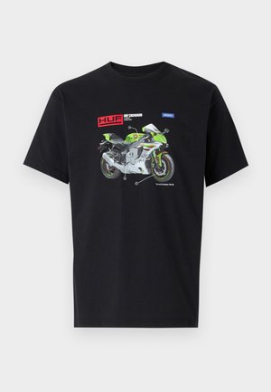 Black cotton t-shirt featuring a graphic design of a green and white motorcycle with labeled parts and "HUF" branding above.
