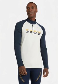 Langärmeliges Sportshirt mit halbem Reißverschluss, cremefarbenem Körper, dunkelblauen Ärmeln und dem Schriftzug "SNOW" in Gelb und Schwarz. Weicher, dehnbarer Stoff.