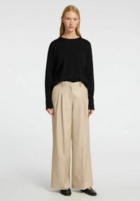 Černý svetr s dlouhým rukávem v kombinaci s béžovými širokými kalhotami. Materiál vypadá jemně a kalhoty mají předn í záhyby a volný střih.
